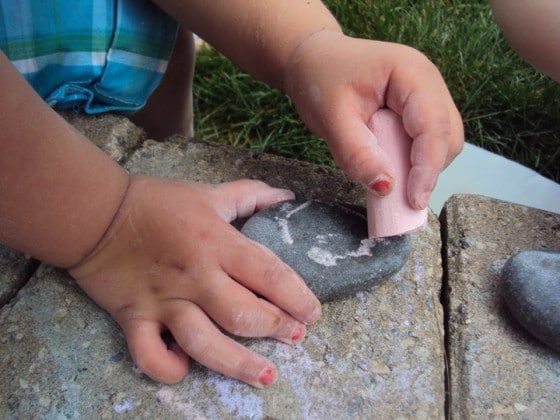 preschooler drawing with chalk on a stone