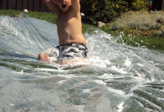 boy in bathing suit sliding on tarp in backyard