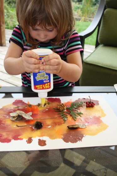toddler gluing fall leaves to smoosh painted backdrop for collage
