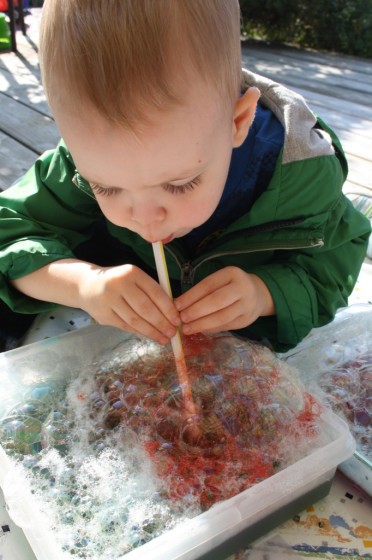 toddler blowing coloured bubbles to make bubble painting