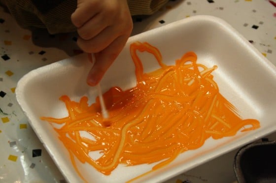preschooler making marks in orange paint with Q-tip