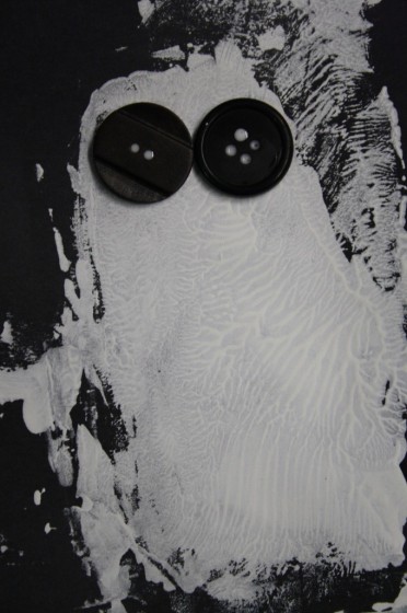 white paint ghost on black paper with black button eyes