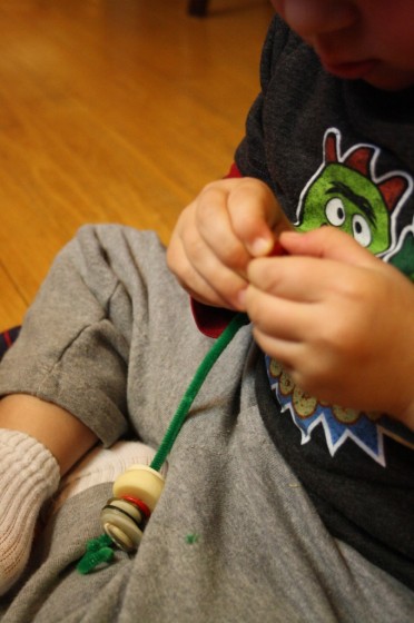 preschooler threading buttons on pipe cleaner