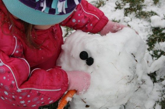toddler putting carrot nose on snowman