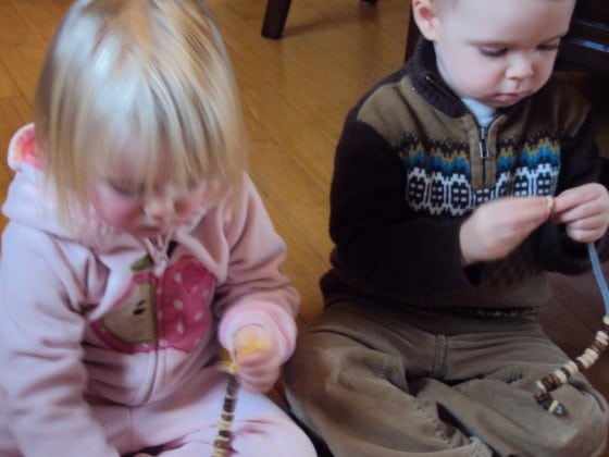 2 toddlers putting cheerios on pipe cleaners