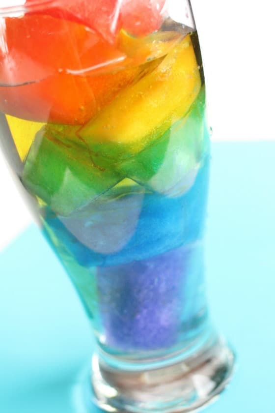 Coloured Ice Cubes layered in rainbow order in glass of water