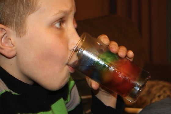 boy drinking glass of water with rainbow coloured ice cubes