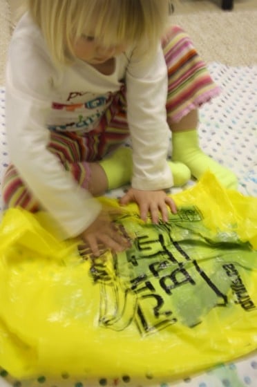 toddler smooching paint on paper in yellow plastic bag