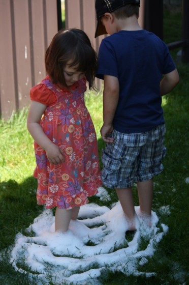 toddler and preschooler standing in soapy water on grass