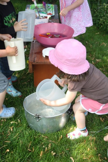 Toddlers and Preschoolers filling pitchers of water in the garden for science learning