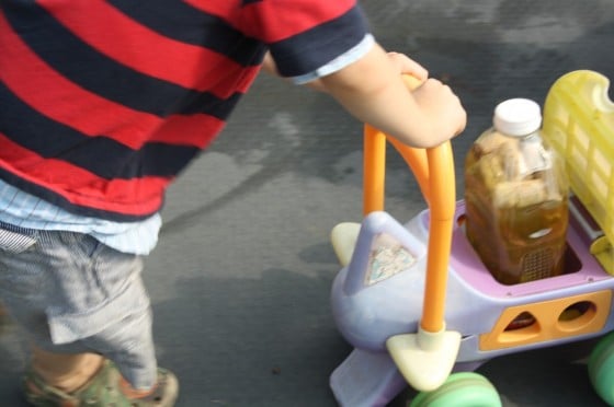 2 year old boy pushing bottle baby in ride on toy