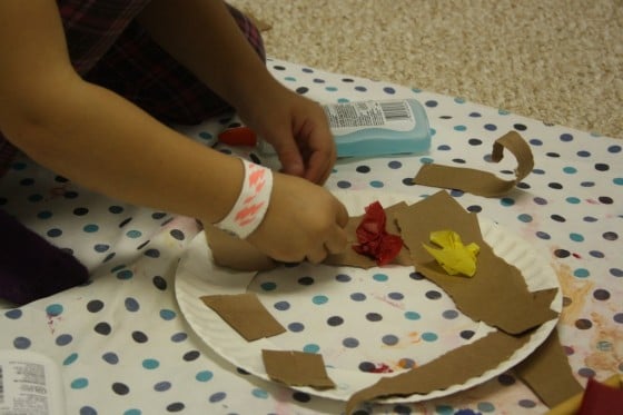 preschooler gluing crumpled tissue paper to paper plate fall wreath 