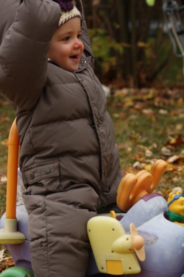 toddler in snow suit on ride on toy in leaves