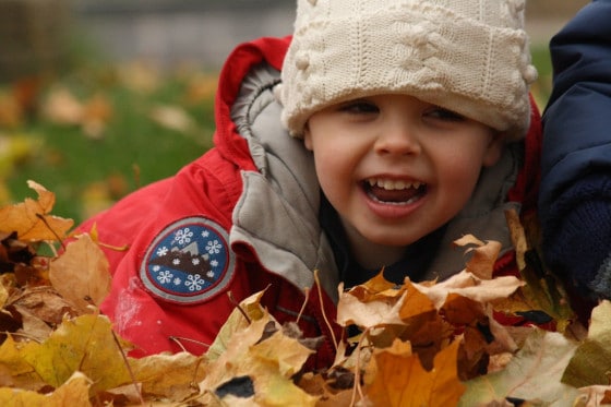 smiling toddler boy laying in fall leaves