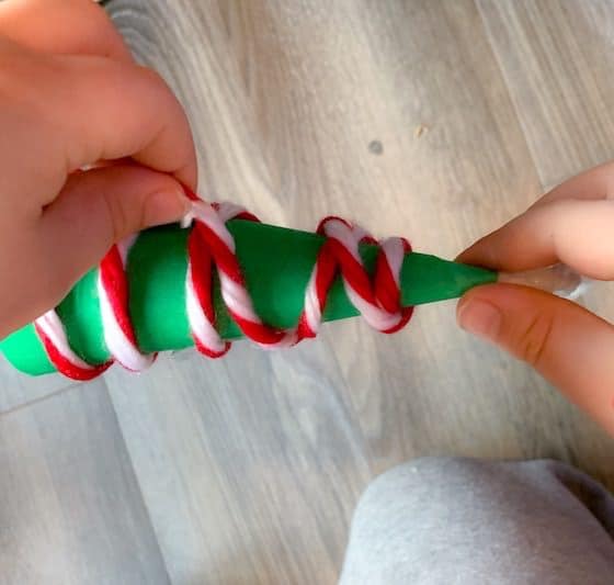 kid wrapping yarn around paper cone christmas tree