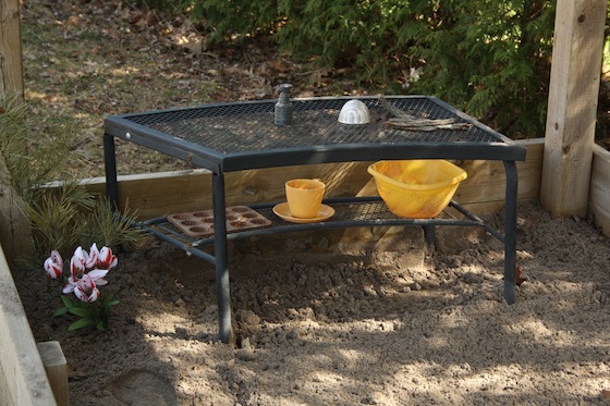 Bench in sandbox holding bowls, cups and artificial flowers