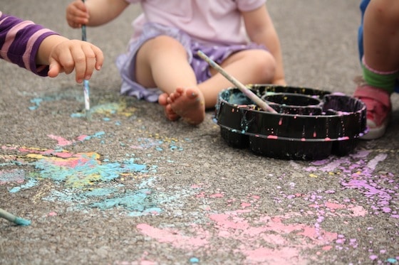 close up toddlers painting with chalk paint in driveway