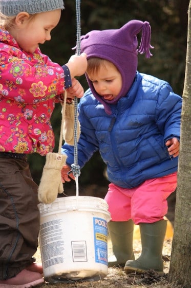 toddlers lifting plastic bucket on rope

