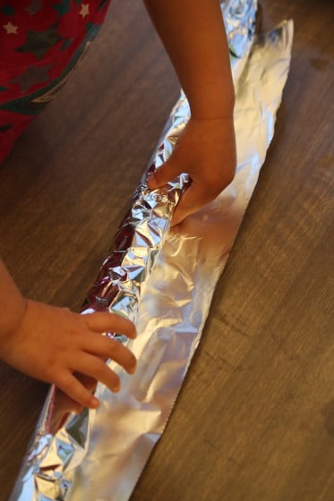 preschooler wrapping cardboard roll with tin foil
