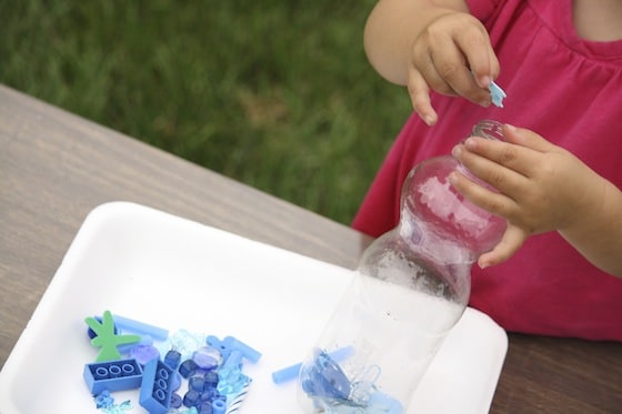 child dropping blue items into plastic bottle