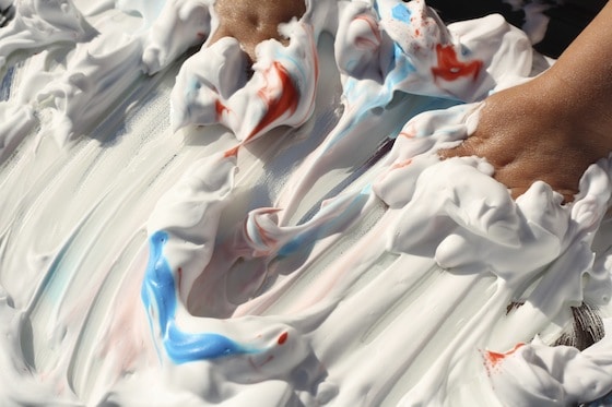 rubbing their hands through blue and red food colouring in the shaving cream
