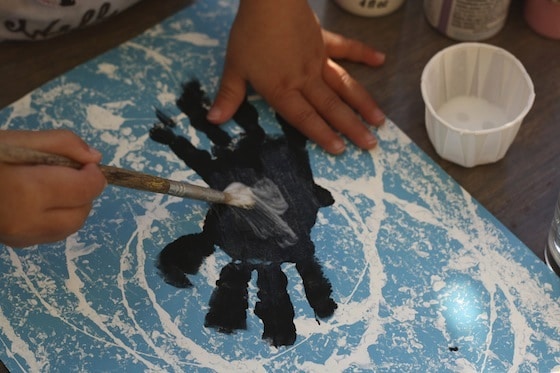 applying glue with a paintbrush to the handprint spiders
