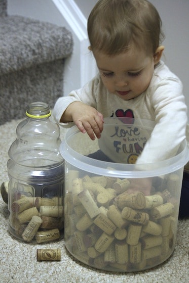 Baby dropping corks into a jug to develop fine motor skills