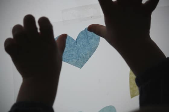 toddler sticking tissue hearts on contact paper window