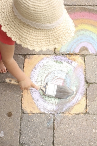 child painting with water over sidewalk chalk drawing