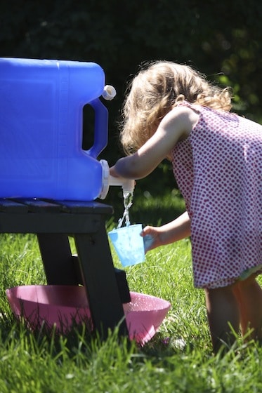 toddler pouring water from camping water carrier