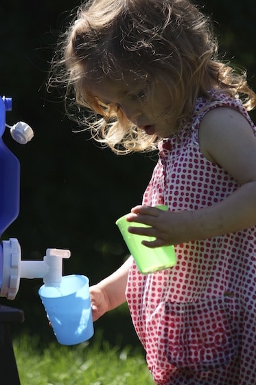 Toddler filling cups from camping jug of water