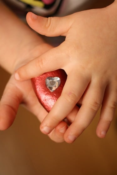Preschoolers hands holding red good luck stone with silver heart