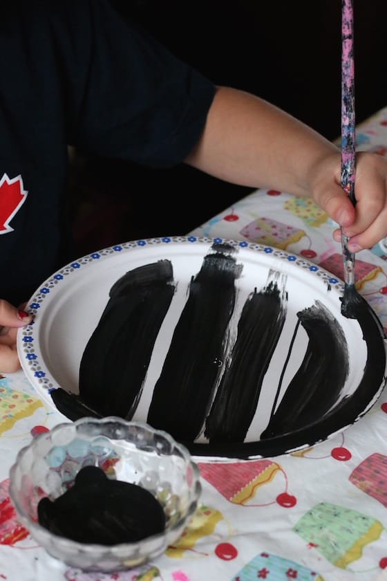 child painting zebra stripes on a paper plate