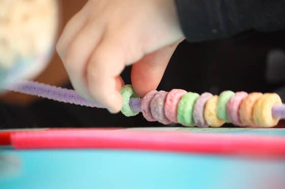 child threading fruit loops onto pipe cleaner