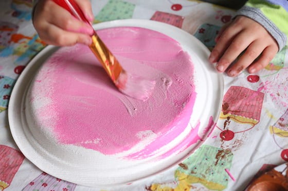 Child painting paper plate with pink paint