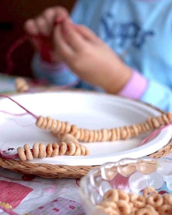 child threading cheerios onto raffia to make homemade bird feeder