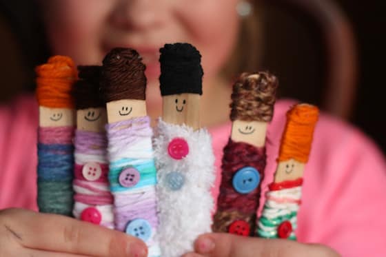 Child holding 5 dolls made with craft sticks and yarn