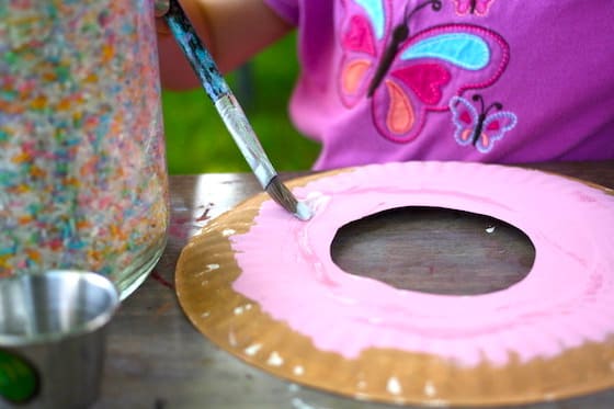child painting pink icing on a paper plate donut