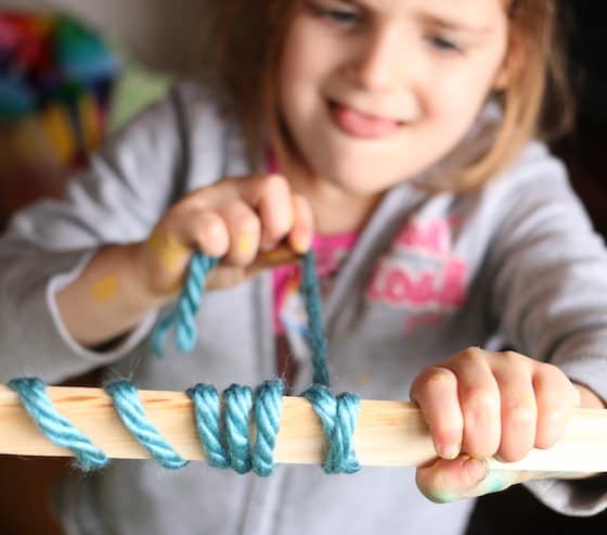 child wrapping blue yarn around paint stick.