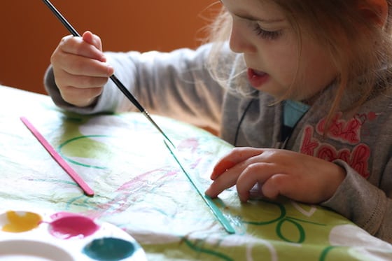 little girl painting wooden stir stick
