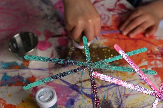 child adding glitter to painted stir sticks