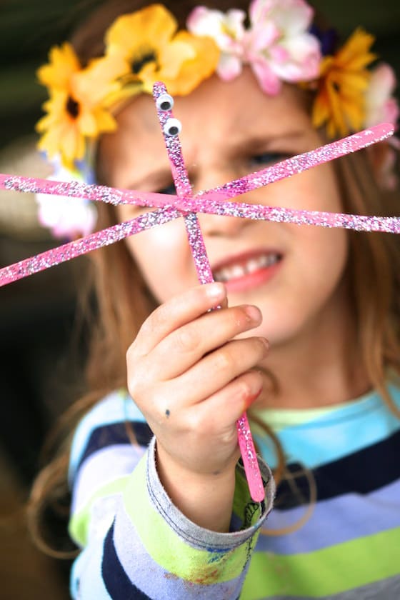 child holding glittered stir stick dragonfly in front of her face