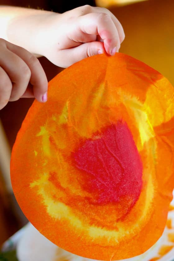 child holding up red yellow and orange coffee filter