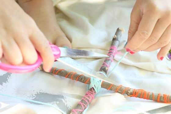 child's hands wrapping-sticks-with-yarn