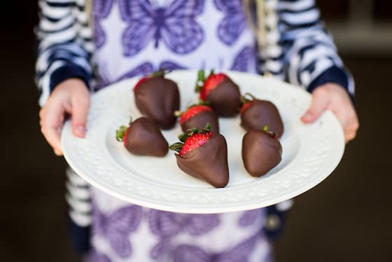 Child holding plate of chocolate covered strawberries