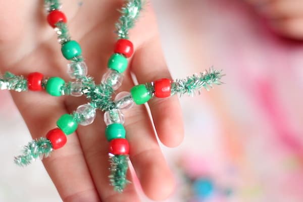 Child's hand holding red and green beaded pipe cleaner snowflake