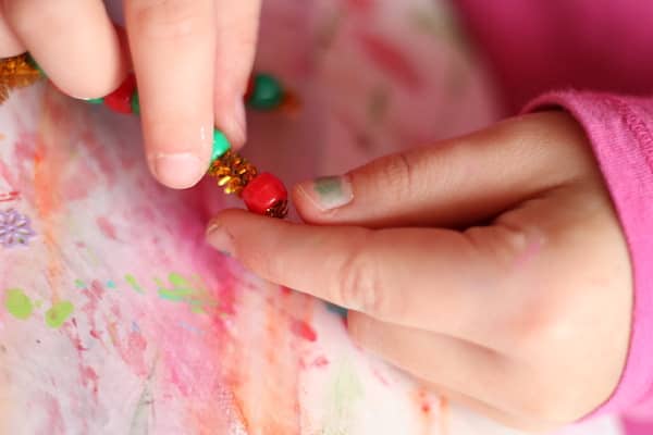 child's hands threading red bead on gold pipe cleaner