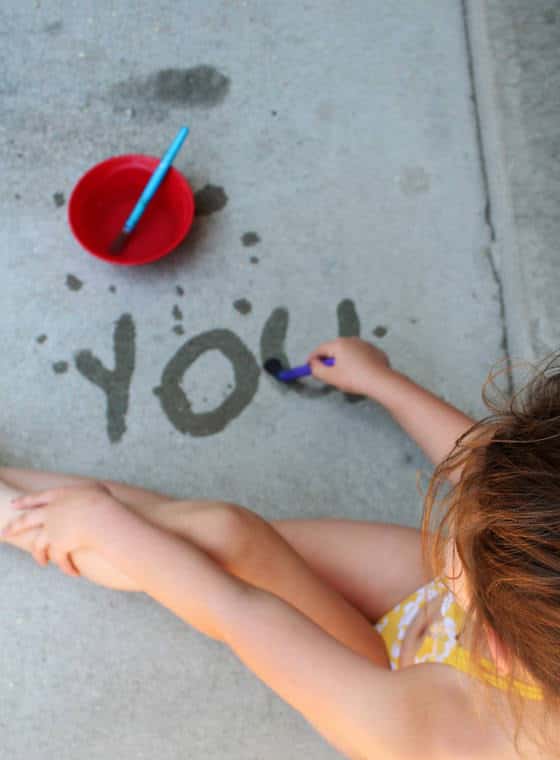Girl practicing her letters by painting letters on the concrete with water. 