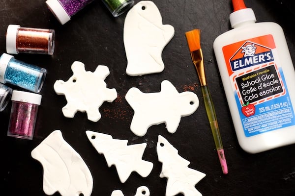 white clay ornaments in cookie cutter shapes beside glitter and white glue