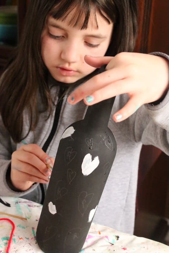 child painting hearts on wine bottle